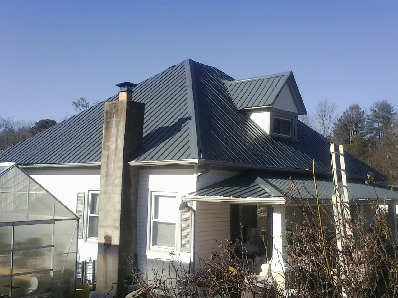 Dark blue standing seam metal roof on a white farmhouse with dormer — Slate & Tile Roof Repair by Roofing Brothers in Minor Hill