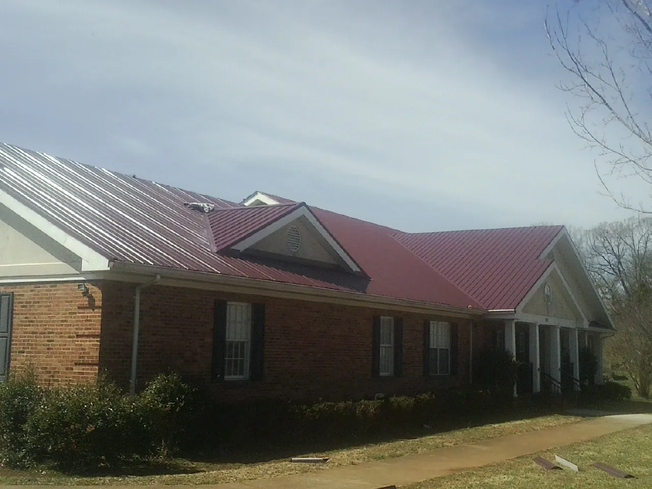 Red metal roof with gabled entries on a long brick building, from a Hail Damage Roof Repair job in Minor Hill
