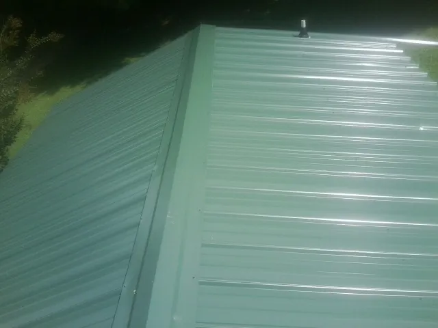 New green metal panels meeting at the ridge of a roof — Flat Roof Repair work by our crew in Minor Hill