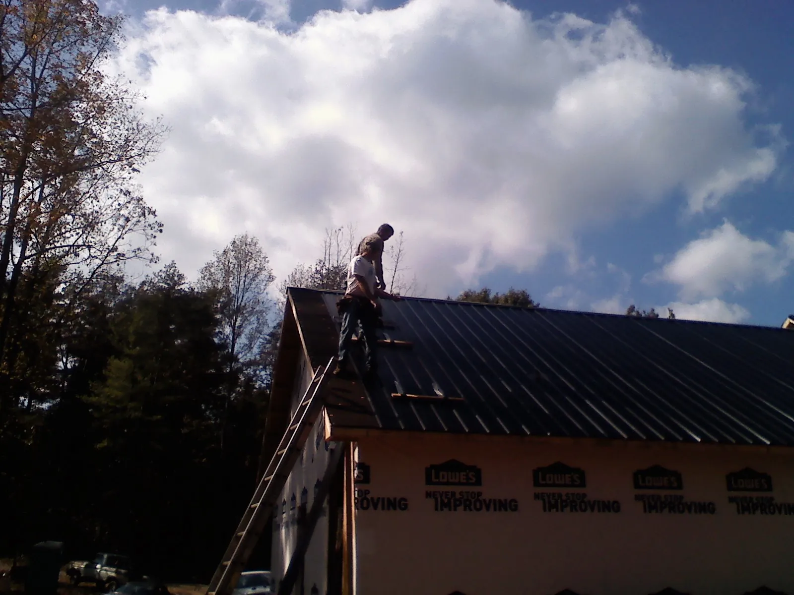 Roofer fastening dark metal panels high against a cloudy sky, from a Roof Inspection job in Minor Hill