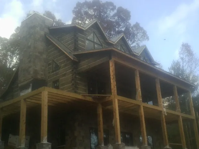 Stone chimney and dormers on a large log home with a timber porch in Minor Hill