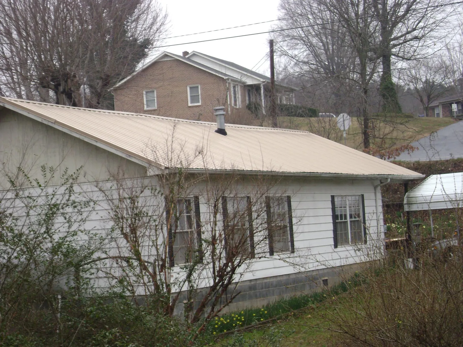 Tan metal roof on a white sided house set into a hillside — Commercial Roofing by Roofing Brothers in Minor Hill