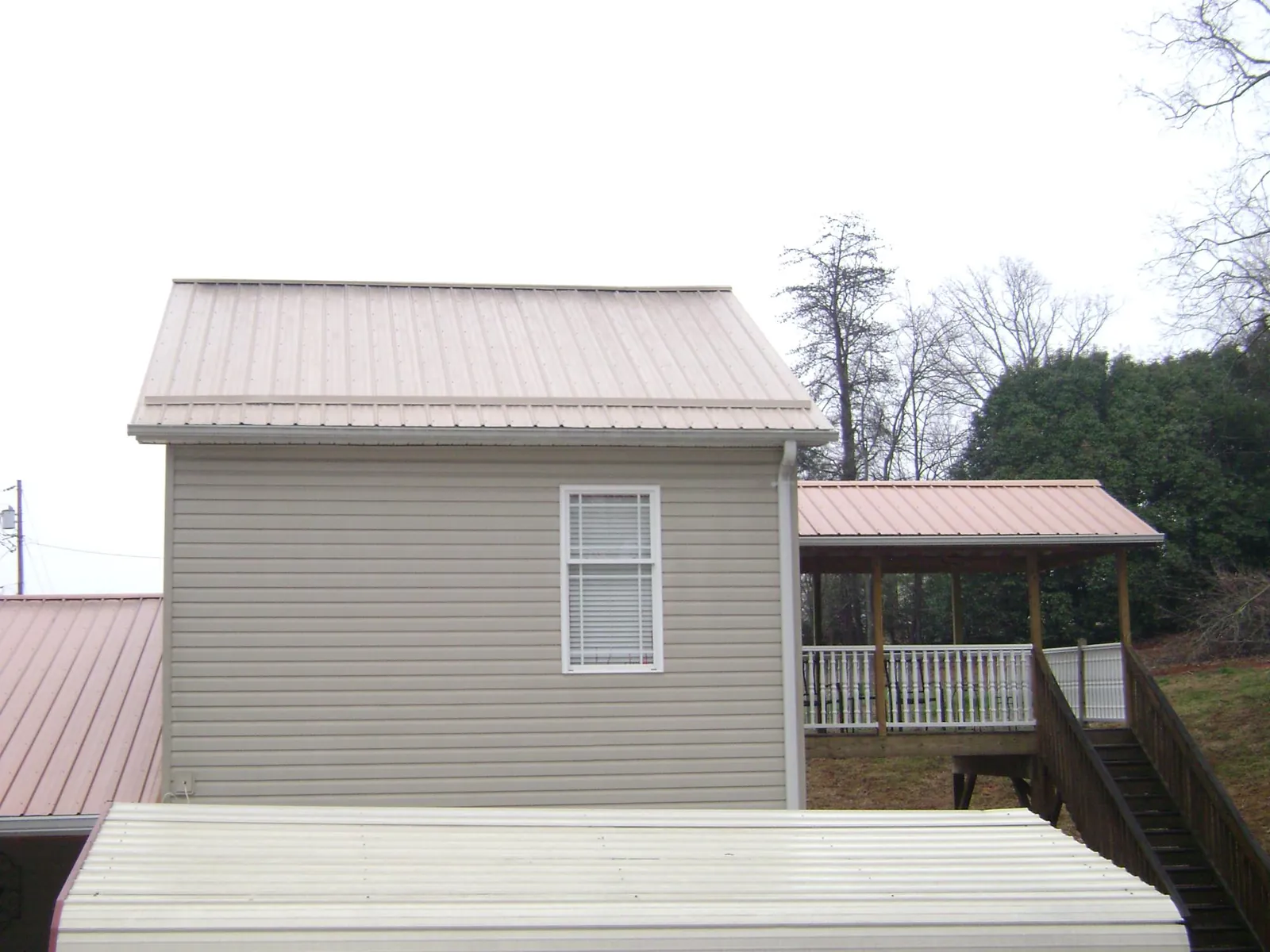 Tan metal roofs on a two story addition and attached porch, from a Roof Replacement job in Minor Hill